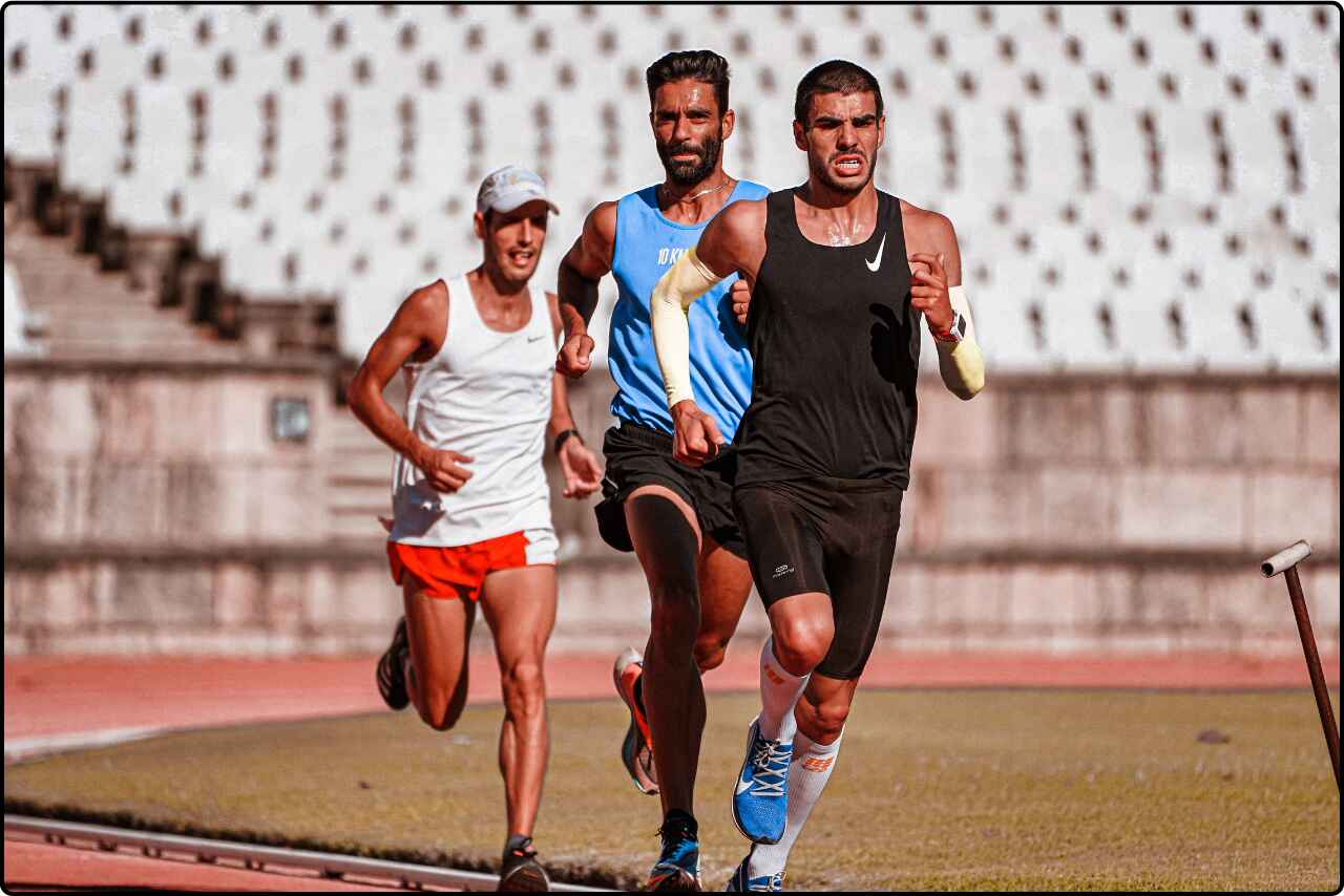 Group of male runners in competitive action on a track.